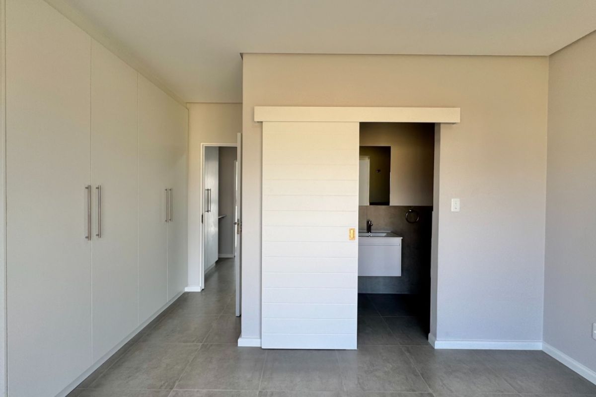 Spacious bedroom featuring modern tiled flooring, extensive built-in cupboards, and a contemporary sliding barn door leading to an en-suite bathroom.