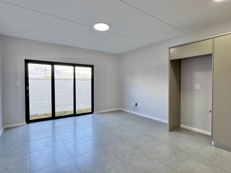 Modern open-plan living area featuring neutral tiled flooring, sleek built-in cabinetry, and large sliding glass doors leading to an outdoor space.