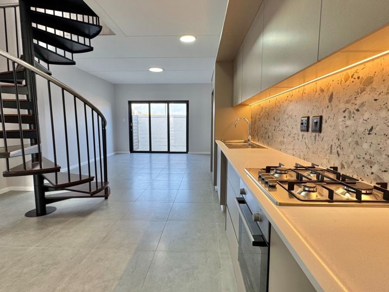 Modern open-plan living area featuring a sleek kitchen with gas hob, terrazzo splashback, and a striking spiral staircase leading to the upper level.