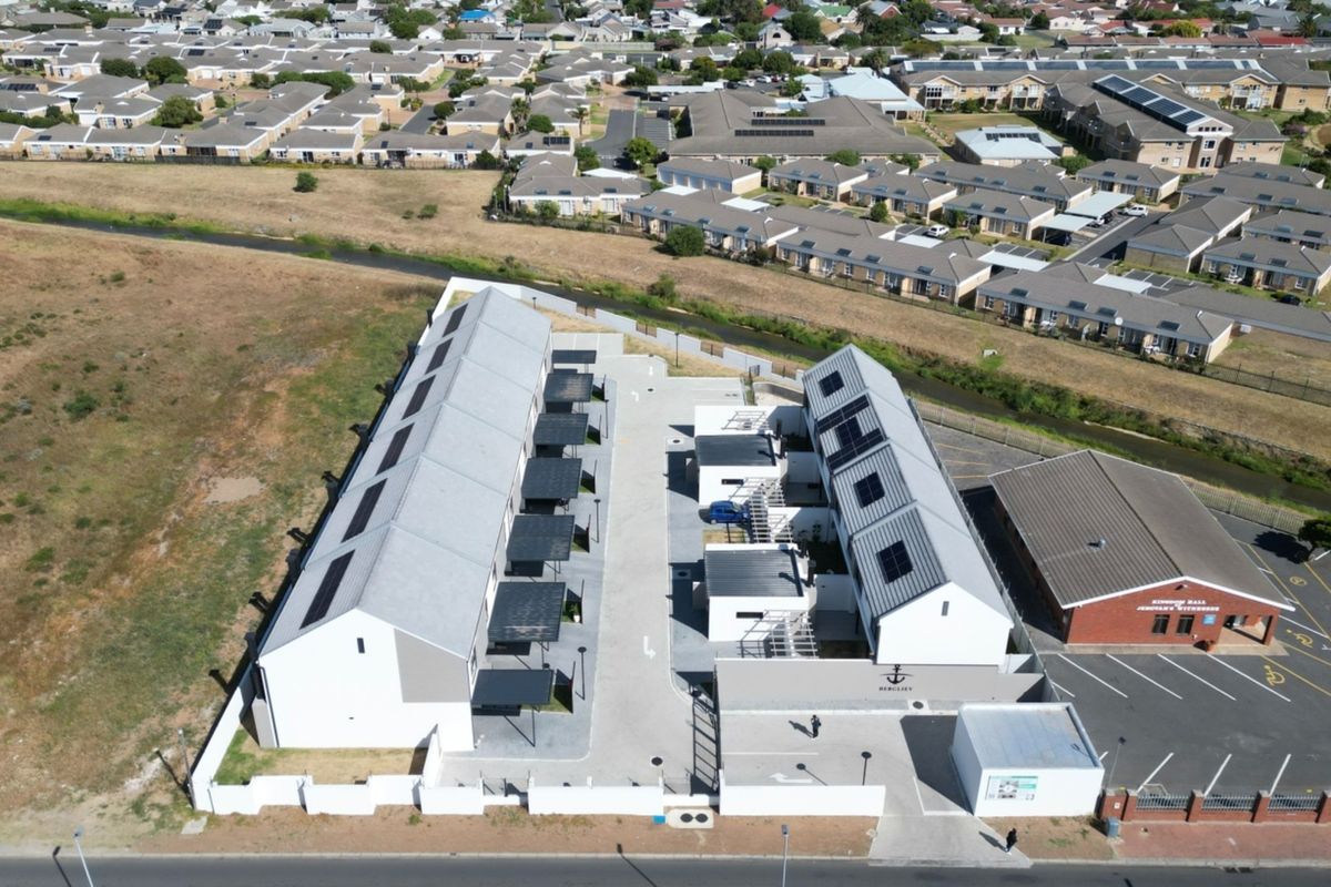 Aerial view of a modern townhouse complex featuring gabled roofs with solar panels, paved driveways, and dedicated carports within a secure perimeter.