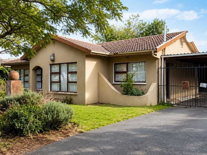 Front elevation of a single-story house featuring a tiled roof, paved driveway, carport, and established garden.