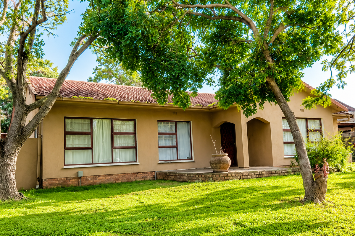 A charming single-story home featuring a tiled roof, brick foundation, and a welcoming covered entrance, set within a well-maintained garden with mature trees.
