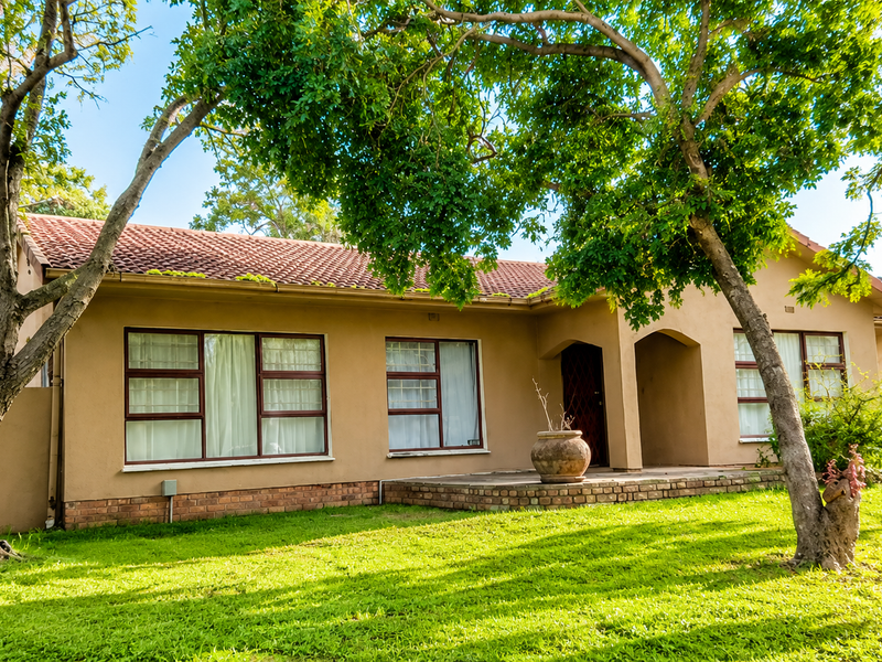 A charming single-story home featuring a tiled roof, brick foundation, and a welcoming covered entrance, set within a well-maintained garden with mature trees.