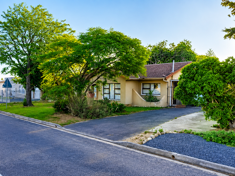 Front view of a single-story residential house featuring a paved driveway, established garden, and tiled roof, situated in a quiet suburban street.
