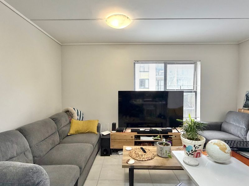 A comfortable living room featuring tiled flooring, a central ceiling light, and a window fitted with venetian blinds.