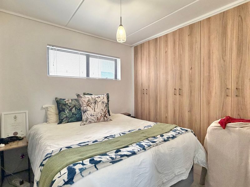 A well-maintained bedroom featuring extensive floor-to-ceiling built-in wooden cupboards, a horizontal window with blinds, and a modern pendant light fixture.
