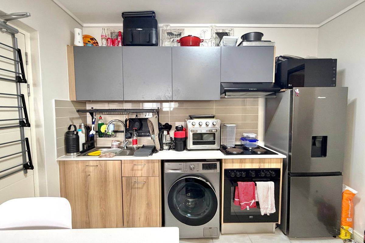 Compact kitchen featuring modern wood-grain lower cabinetry, grey upper cabinets, tiled backsplash, built-in oven, hob, extractor fan, and an integrated washing machine.