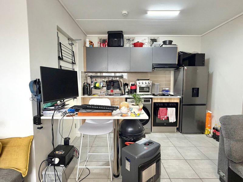 Compact open-plan kitchen featuring modern cabinetry, built-in oven, extractor fan, and tiled flooring, integrated into a functional living space.