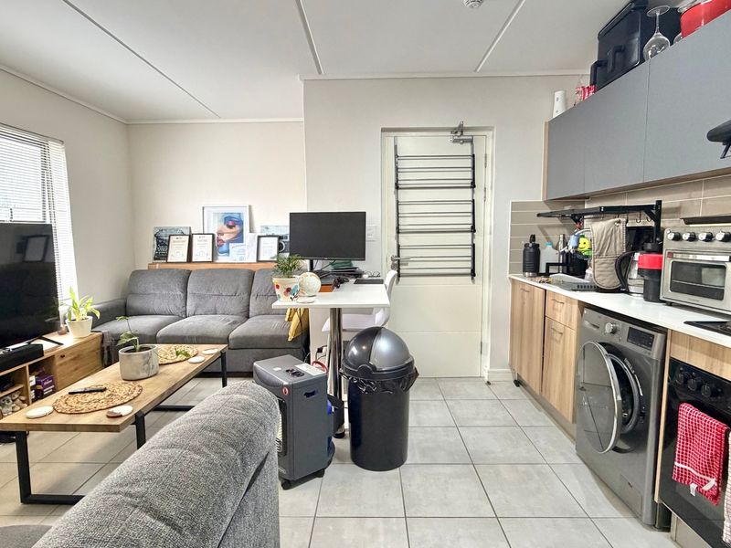 Open-plan living area featuring a compact kitchen with built-in cabinetry, oven, hob, and integrated laundry facilities, seamlessly connected to the lounge space.