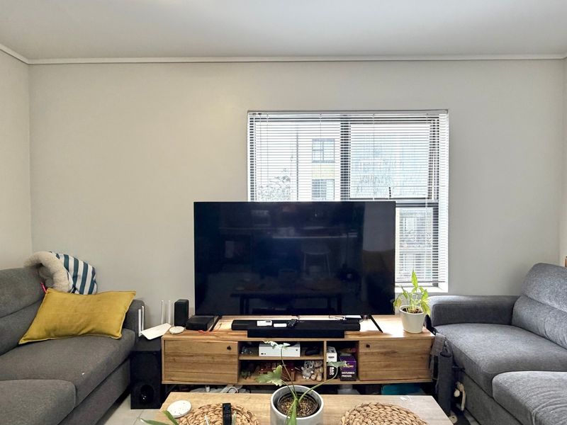A comfortable living room featuring a central window with fitted venetian blinds, providing natural light to the space.