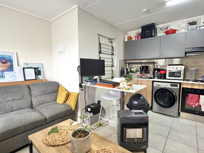 Open-plan living area featuring a compact kitchen with built-in cabinetry, integrated oven, extractor fan, and tiled flooring throughout.