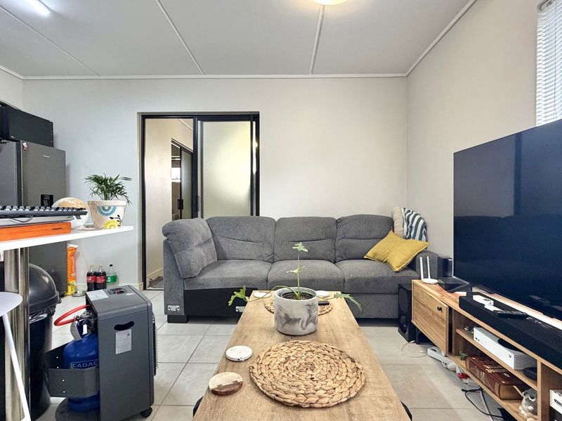 Open plan living area featuring tiled flooring, a compact kitchen section with built-in cabinetry, and a sliding door leading to an adjacent room.