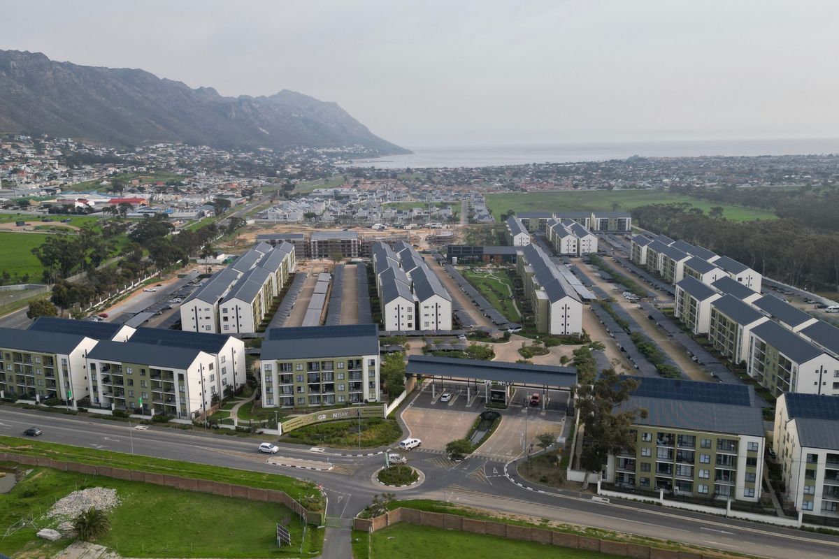 Aerial view of a modern residential apartment complex featuring multiple buildings, secure gated access, solar installations, and landscaped surroundings with mountain and coastal views.