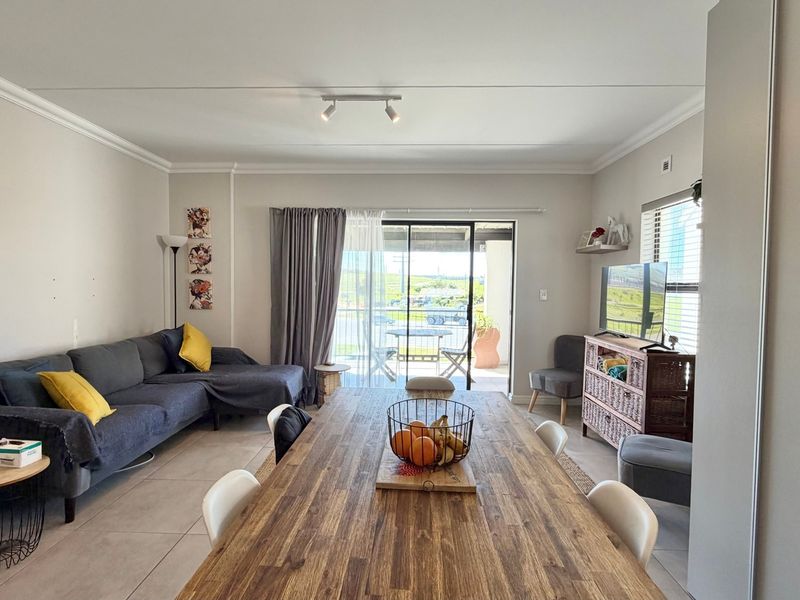 An open-plan living and dining area featuring tiled flooring, cove cornicing, and a large sliding glass door providing access to an outdoor patio.
