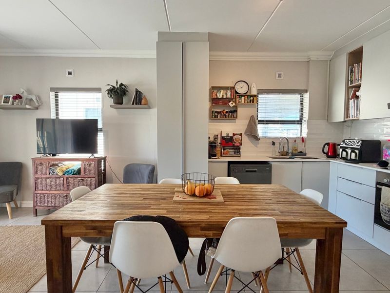 An open-plan living and kitchen area featuring modern cabinetry, a built-in oven, subway tile backsplash, and tiled flooring throughout.
