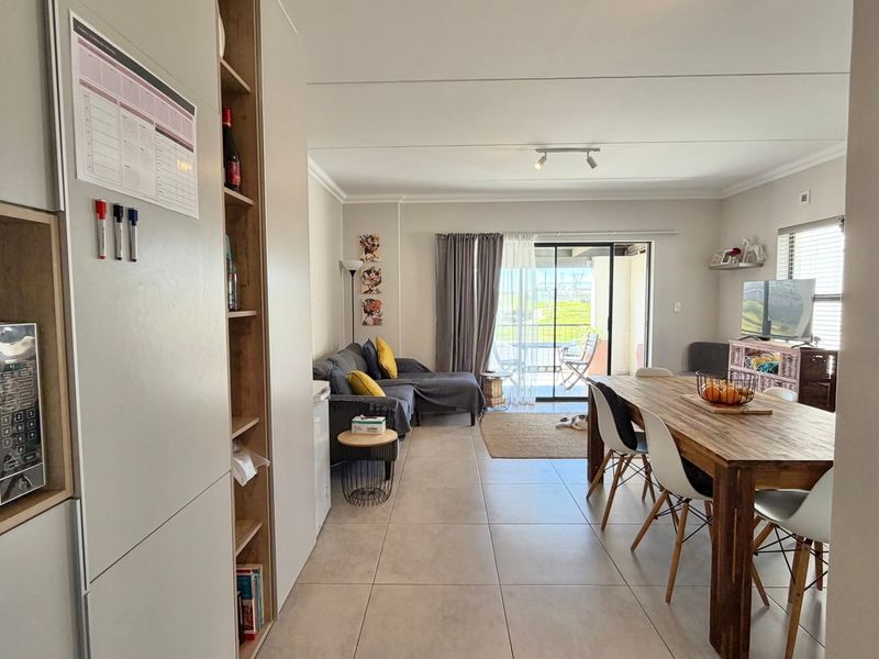 Open-plan living and dining area featuring neutral tiled flooring, built-in cabinetry, and a sliding glass door leading to an outdoor patio space.