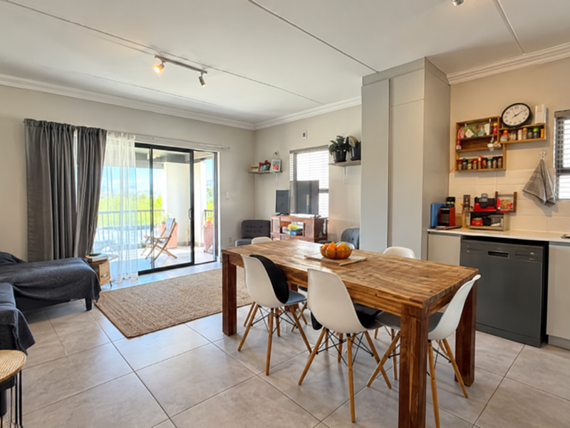 Open-plan living and dining area featuring tiled floors, a modern kitchen with integrated appliances, and sliding doors leading to a private balcony.