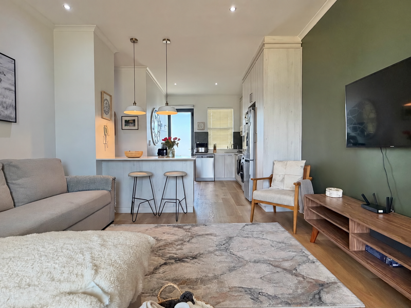 A bright open-plan living and kitchen area featuring modern cabinetry, a central island with pendant lighting, and stylish wood-look flooring.