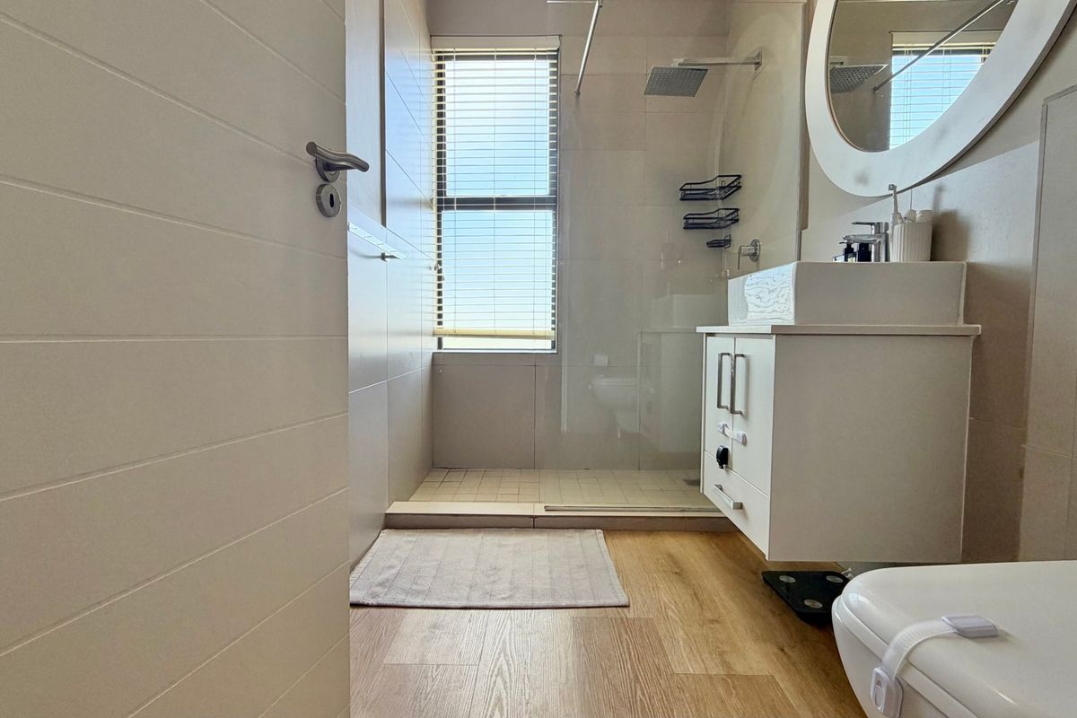 Modern bathroom featuring a walk-in shower with glass screen, wall-mounted vanity with vessel sink, and neutral tiling throughout.