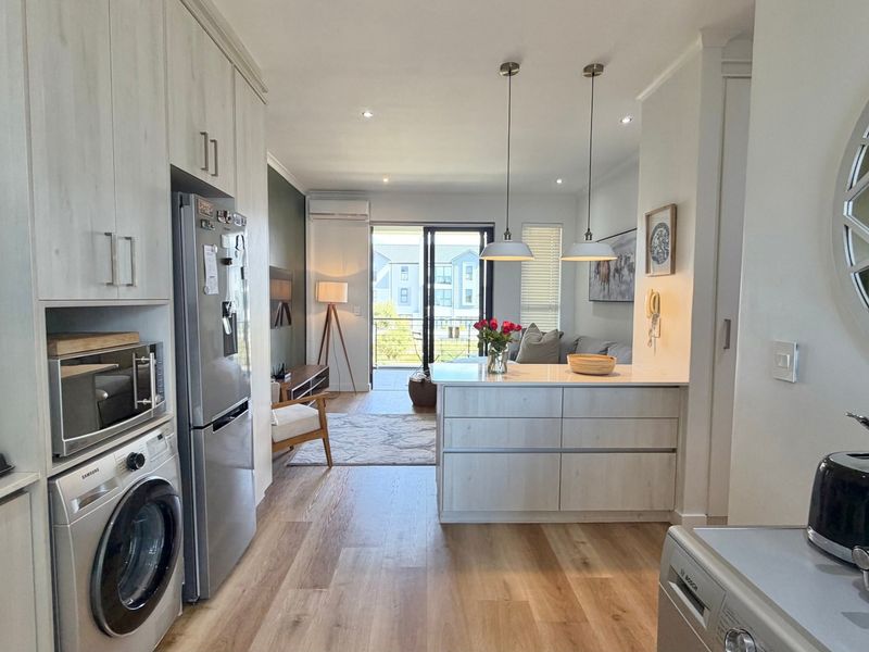 Modern open-plan living area featuring a well-appointed kitchen with built-in cabinetry, a central island, and seamless flow to a balcony through sliding glass doors.