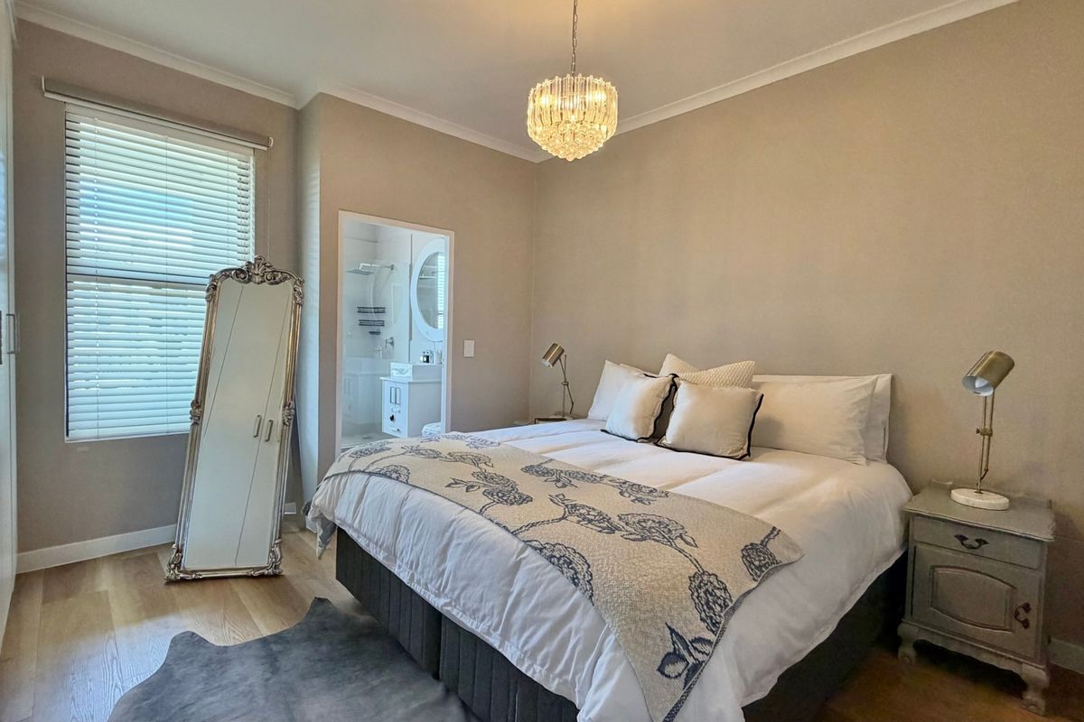 A well-maintained bedroom featuring laminate flooring, built-in cupboards, venetian blinds, and direct access to an en-suite bathroom.
