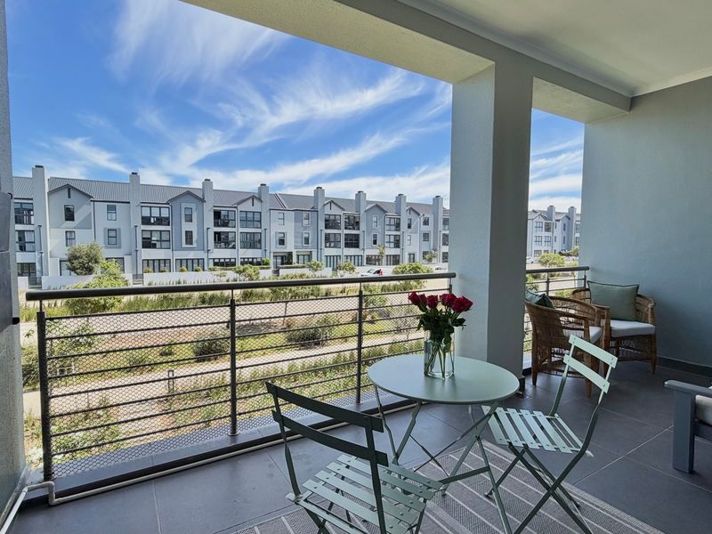 A modern covered balcony featuring tiled flooring and a secure metal mesh balustrade, offering an open view of the surrounding residential complex.