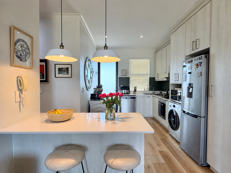 Modern kitchen featuring light-toned cabinetry, stone countertops, integrated appliances, and a breakfast bar with pendant lighting, creating a functional and bright culinary space.