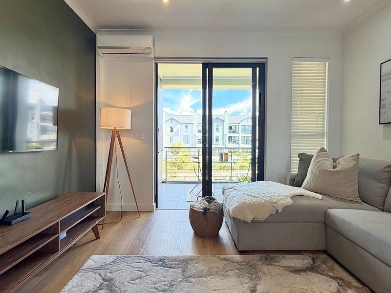 Modern living room featuring timber flooring, air conditioning, and large sliding glass doors opening onto a private balcony.