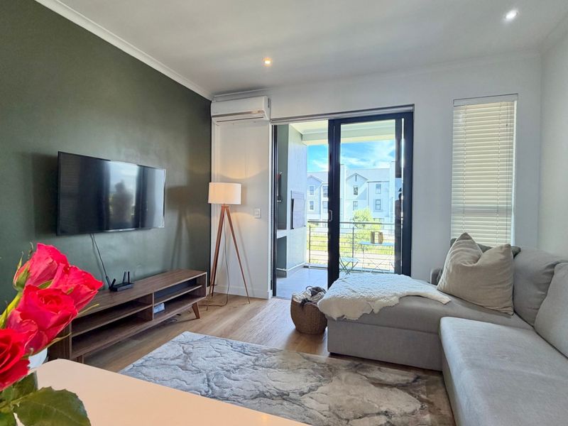 A well-maintained living room featuring laminate flooring, recessed lighting, a split-system air conditioner, and direct access to a private balcony through sliding glass doors.