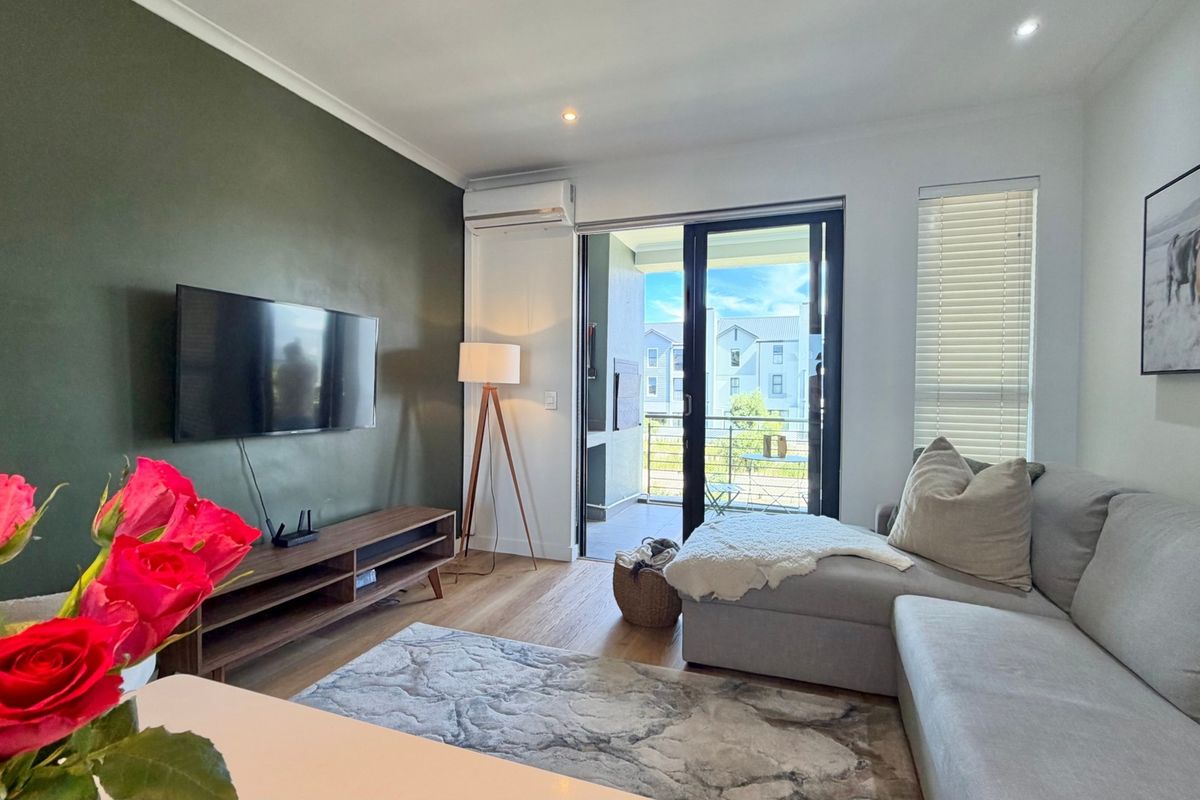 A well-maintained living room featuring laminate flooring, recessed lighting, a split-system air conditioner, and direct access to a private balcony through sliding glass doors.
