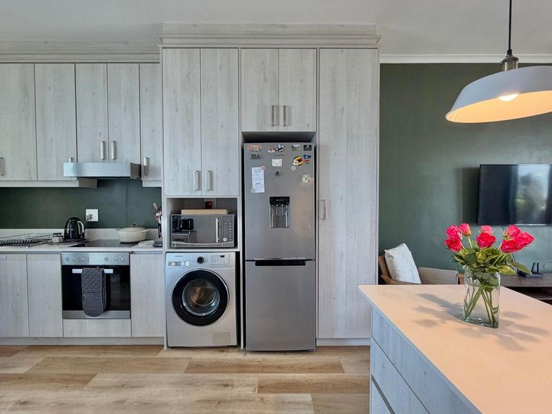 Modern open-plan kitchen featuring light wood-grain cabinetry, integrated appliances, and a functional island, seamlessly flowing into the adjacent living area.