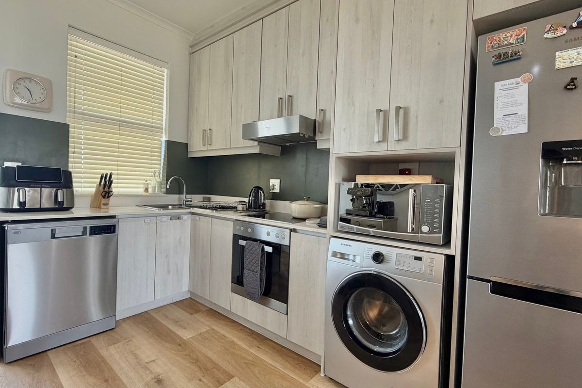 A modern, well-maintained kitchen featuring light wood-grain cabinetry, integrated stainless steel appliances, and laminate flooring with ample storage space.