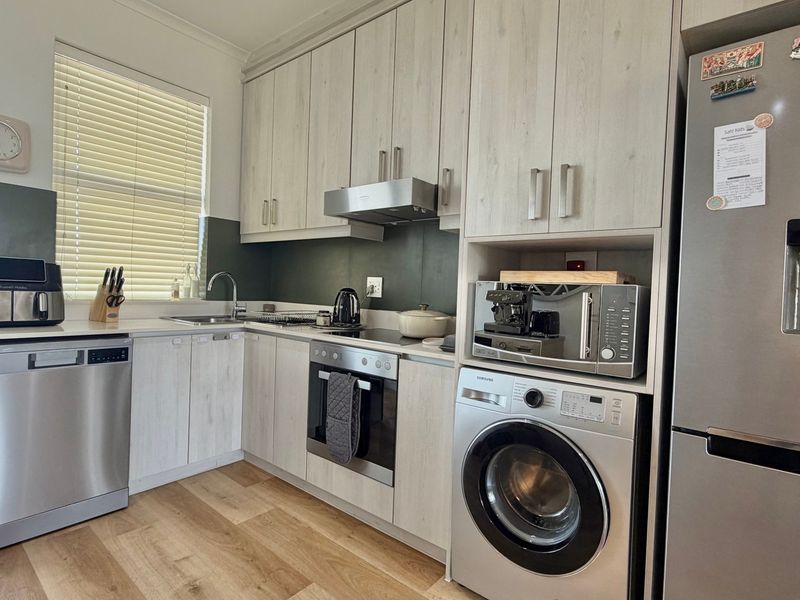 A modern, well-maintained kitchen featuring light wood-grain cabinetry, integrated stainless steel appliances, and laminate flooring with ample storage space.