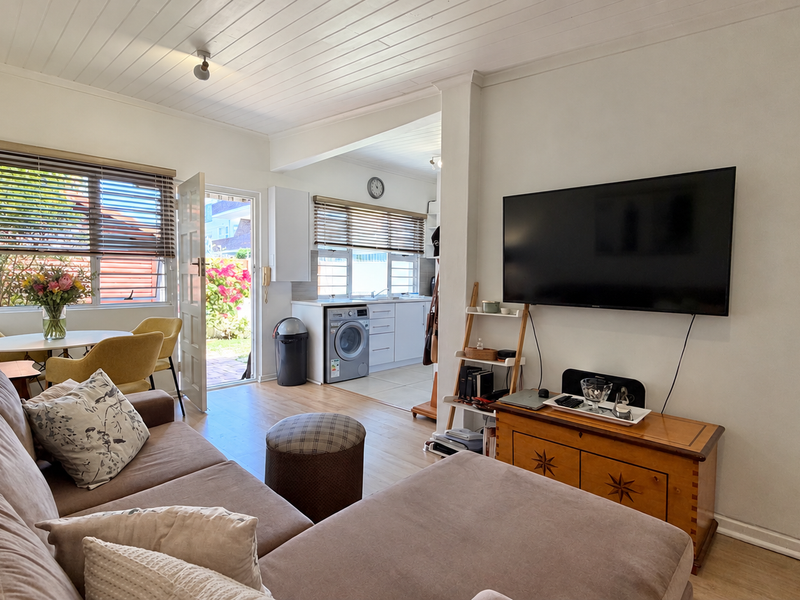 Open-plan living area featuring laminate flooring, timber ceiling, and an integrated kitchen and laundry space with direct access to the rear garden.