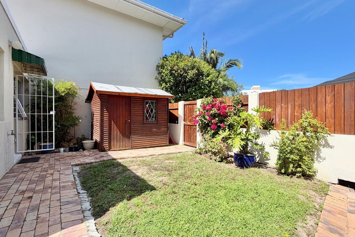 A private rear courtyard featuring brick paving, a wooden garden shed, and a secure timber boundary fence with established garden greenery.