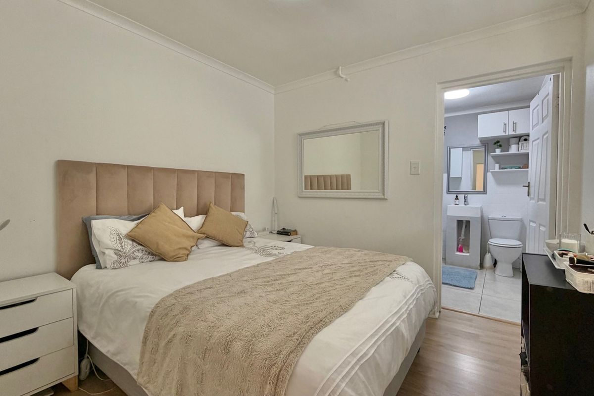A well-maintained bedroom featuring laminate flooring, cove cornicing, and direct access to an en-suite bathroom.