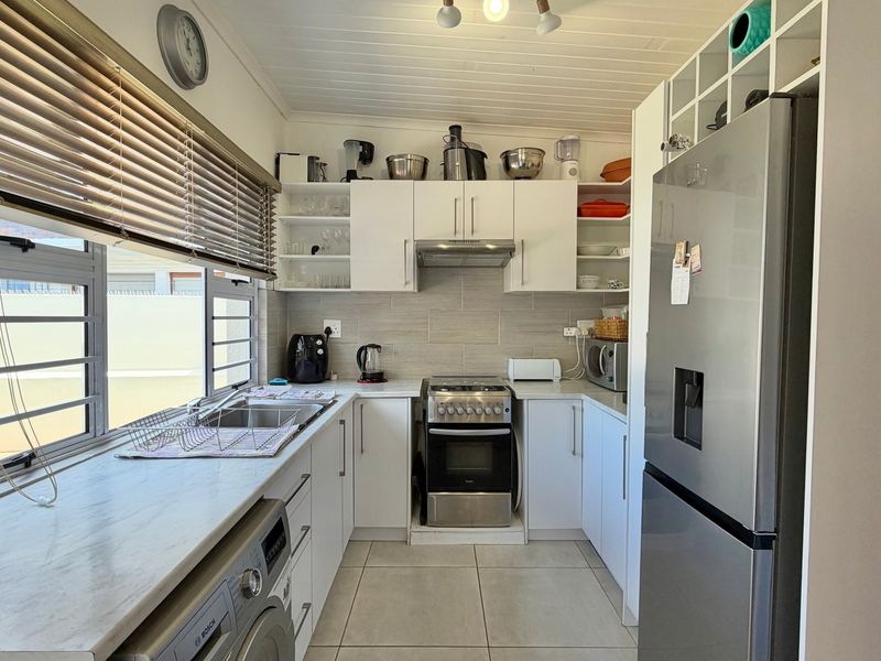 A functional kitchen featuring white cabinetry, stainless steel appliances, tiled backsplash, and a bright window with blinds.