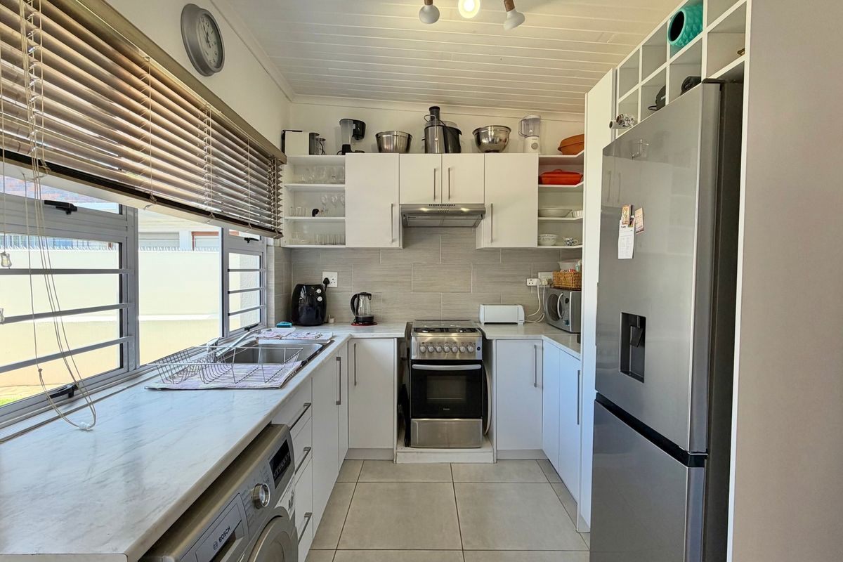 A functional kitchen featuring white cabinetry, stainless steel appliances, tiled backsplash, and a bright window with blinds.