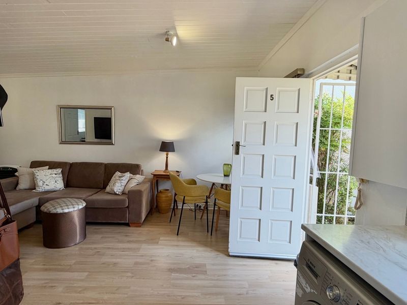 Open-plan living area featuring light timber-look flooring, a panelled ceiling, and direct access to the exterior through a secure entry door.