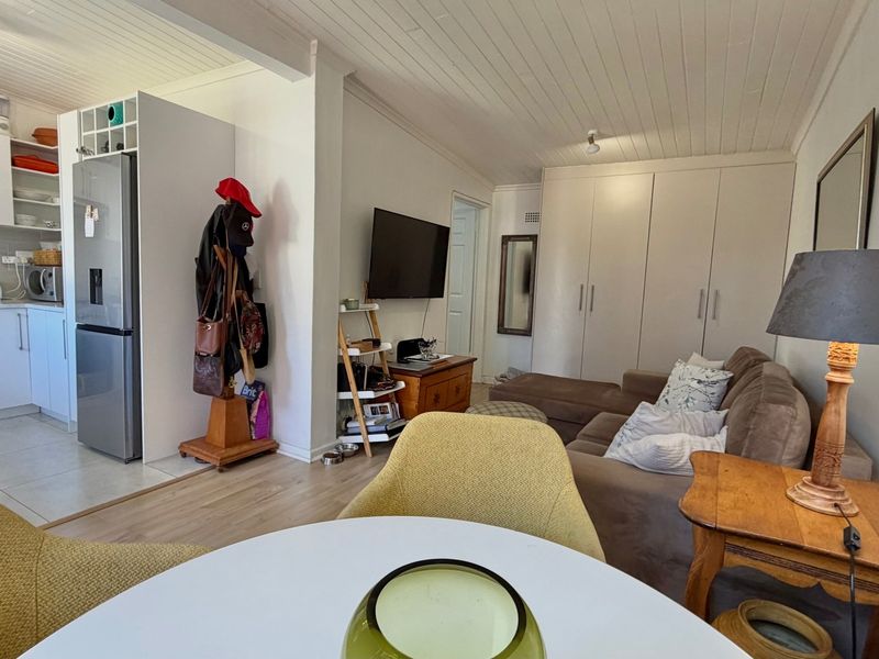 Open-plan living area featuring a compact kitchen with built-in cabinetry and stove, flowing into a lounge space with ample built-in storage cupboards.