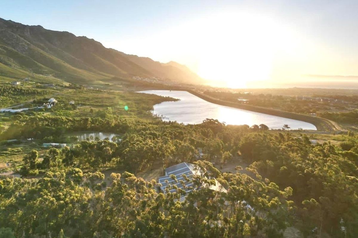 An aerial view of the farm property featuring expansive woodland, a large dam, and scenic mountain vistas at sunset.
