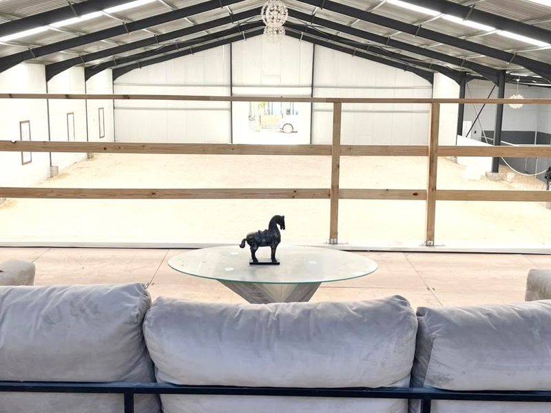An elevated viewing area overlooking a large indoor equestrian arena with exposed steel trusses and a timber safety balustrade.