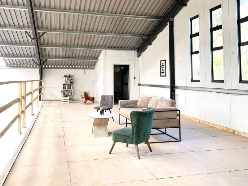 Spacious open-plan living area featuring high vaulted ceilings with exposed steel rafters, large windows, and a timber balustrade overlooking the lower level.