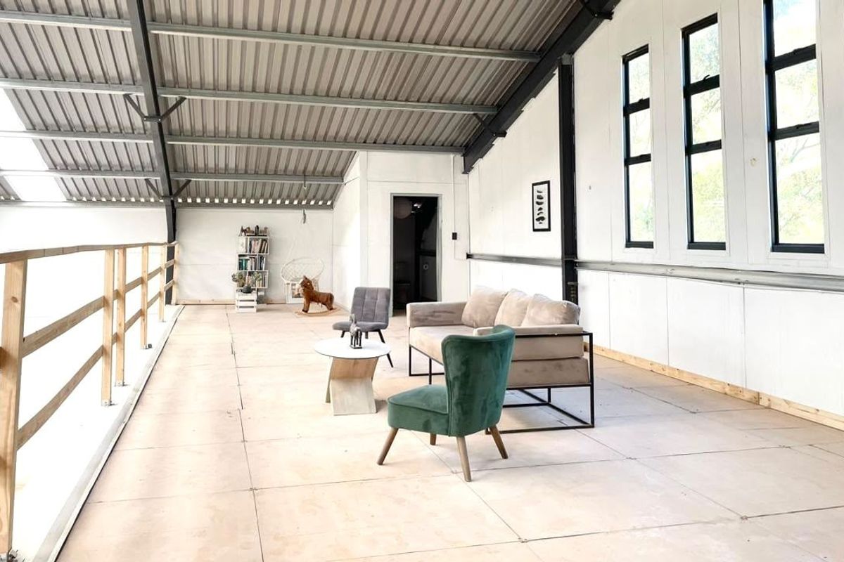 Spacious open-plan living area featuring high vaulted ceilings with exposed steel rafters, large windows, and a timber balustrade overlooking the lower level.