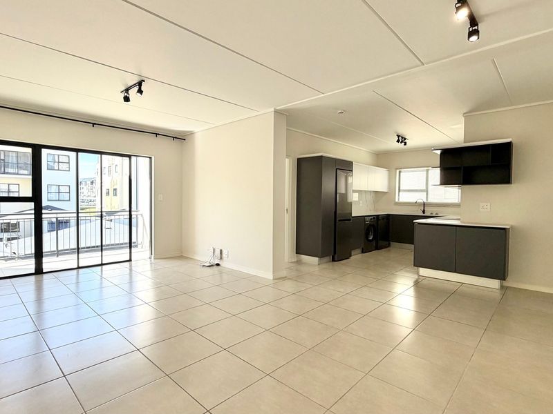 Spacious open-plan living area featuring tiled floors, modern kitchen cabinetry, and direct access to a private balcony through sliding glass doors.