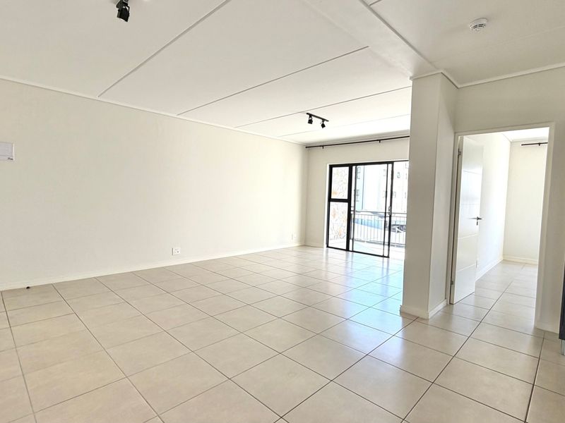 A bright, spacious, and empty living area featuring neutral tiled flooring, modern track lighting, and a sliding glass door leading to an outdoor space.