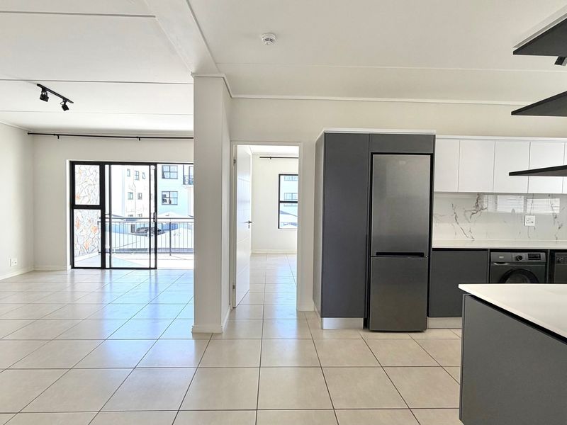 Modern open-plan living area featuring a sleek kitchen with integrated appliances, tiled flooring, and seamless access to a private balcony.