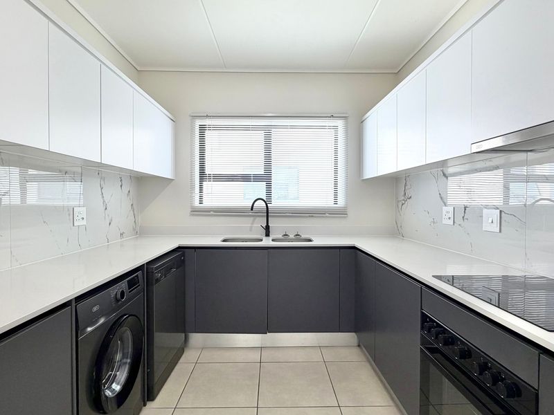 Modern galley-style kitchen featuring sleek dark cabinetry, white countertops, marble-look splashbacks, and integrated appliances including an oven and hob.