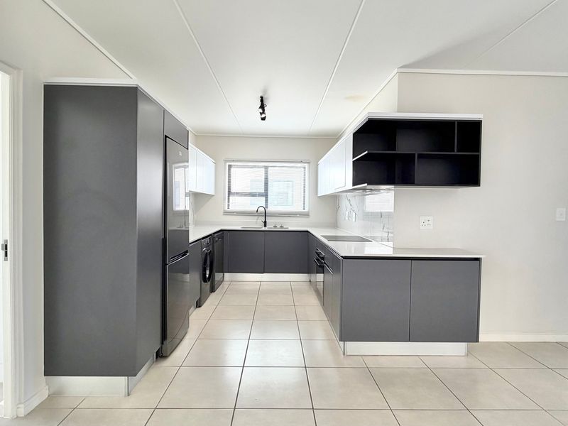 Modern kitchen featuring sleek grey and white cabinetry, stone countertops, integrated appliances, and tiled flooring in a clean, minimalist layout.