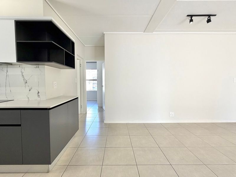 Modern open-plan living area featuring a sleek kitchen with built-in appliances, marble-look splashback, and neutral ceramic floor tiles throughout.